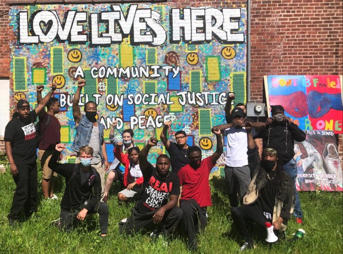 Group with fists raised in front of a Love Lives Here mural